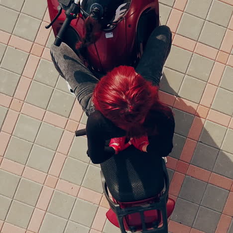 female biker having a rest on her modern vehicle isolated on the pavement background outdoors. beautiful girl with red hair and jeans sitting on a motorbike. camera moves around.