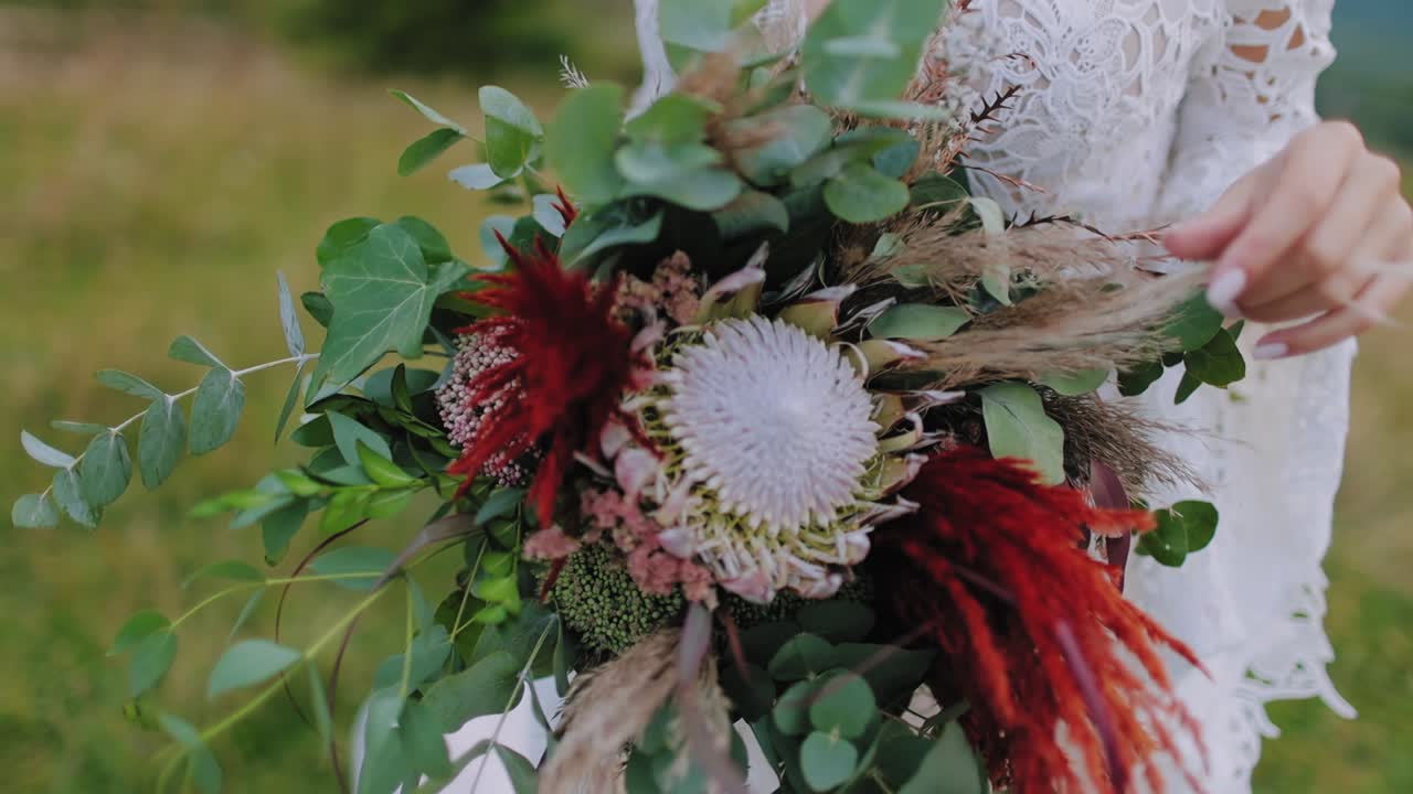 Various flowers in bouquet in woman's hands. Bride in wedding dress holds bunch of exotic flowers on nature background. Close-up.