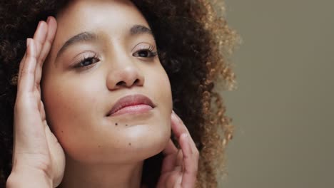 biracial woman with dark hair touching face on beige background, slow motion