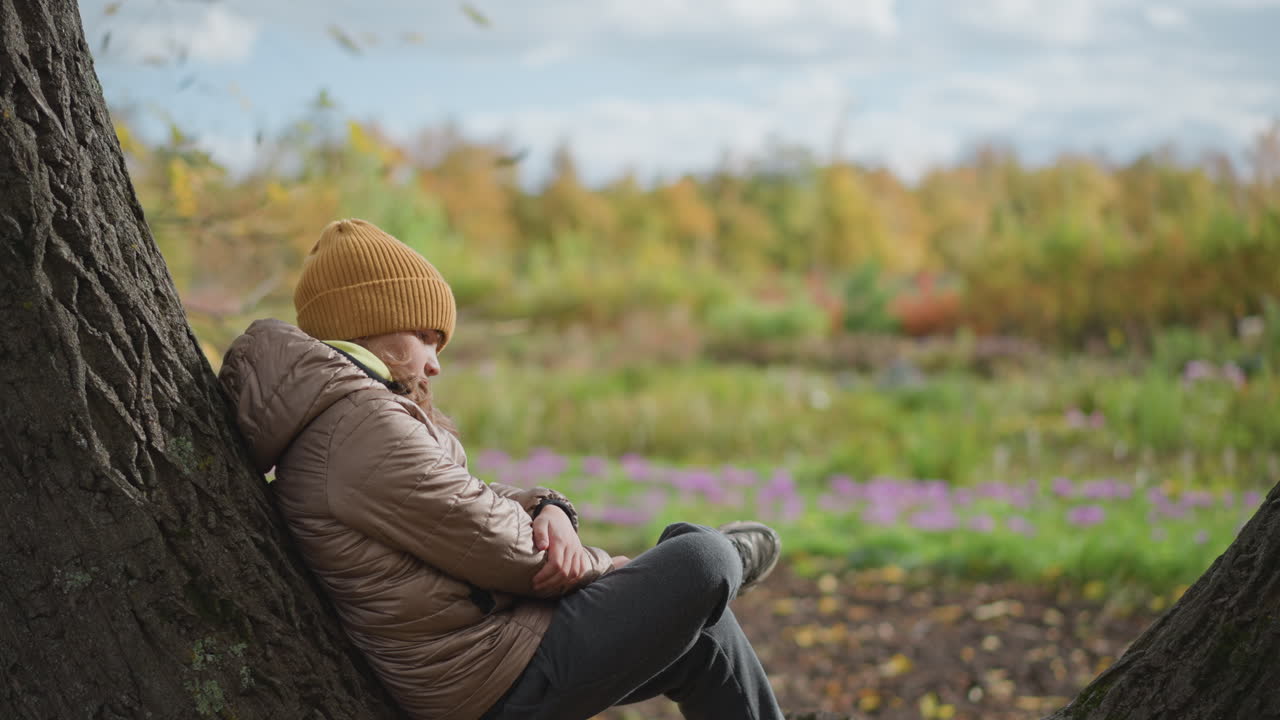 woman approaches daughter sitting on tree trunk and lovingly hands over autumn leaf before leaning in to give warm peck in calm park filled with vibrant fall foliage and soft cloudy sky