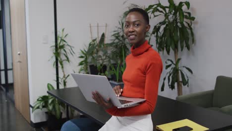 Portrait-of-african-american-woman-smiling-while-using-laptop-at-office