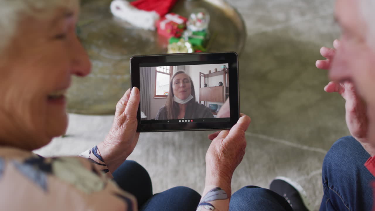 pareja caucásica mayor usando una tableta para una videollamada de navidad con una mujer feliz en la pantalla