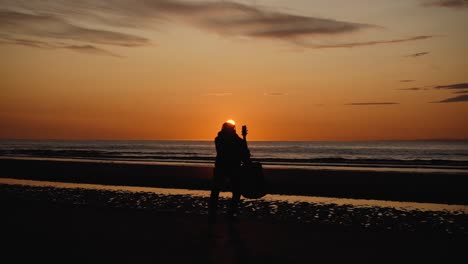 Mann-Läuft-Mit-Gitarre-Im-Hinteren-Sandstrand-Bei-Sonnenuntergang-1