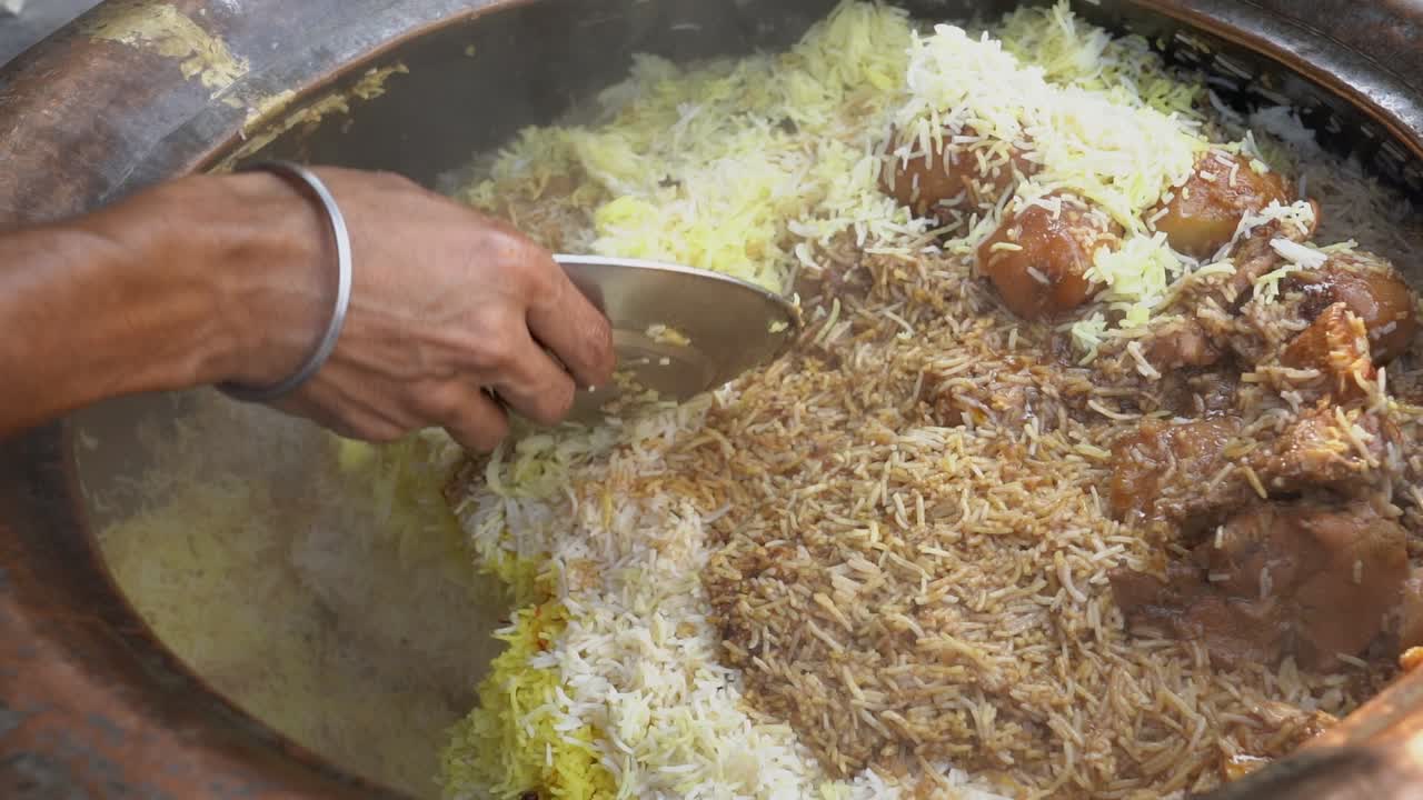 Un vendedor de comida callejera sirve auténtico biryani de pollo indio con arroz basmati con azafrán y patatas de un handi de barro tradicional. Perfecto para documentales de viajes, gastronomía y cultura