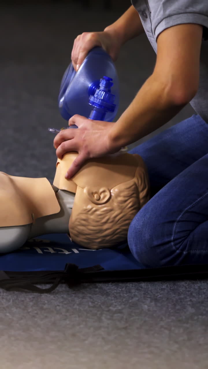 Instructor demonstrates breathing exercise on a mannequin. Woman on a mat on the floor over the dummy giving a medical training. Vertical video