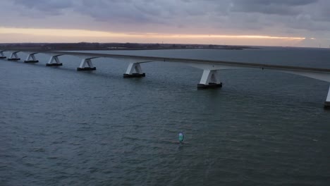 aerial wide shot of a zeelandbrug longest bridge in holland with a surfer on an airfoil with blue wing wind foiling under it