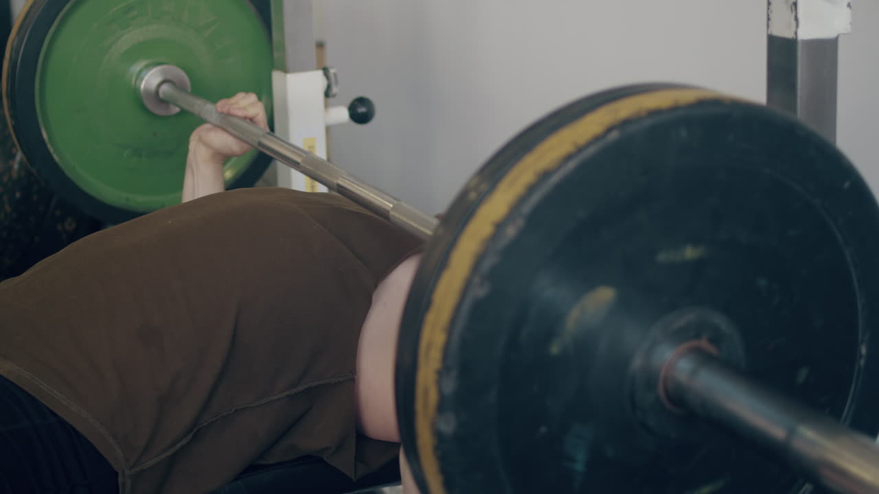Man bench presses several reps then racks weight in gym, slow-mo