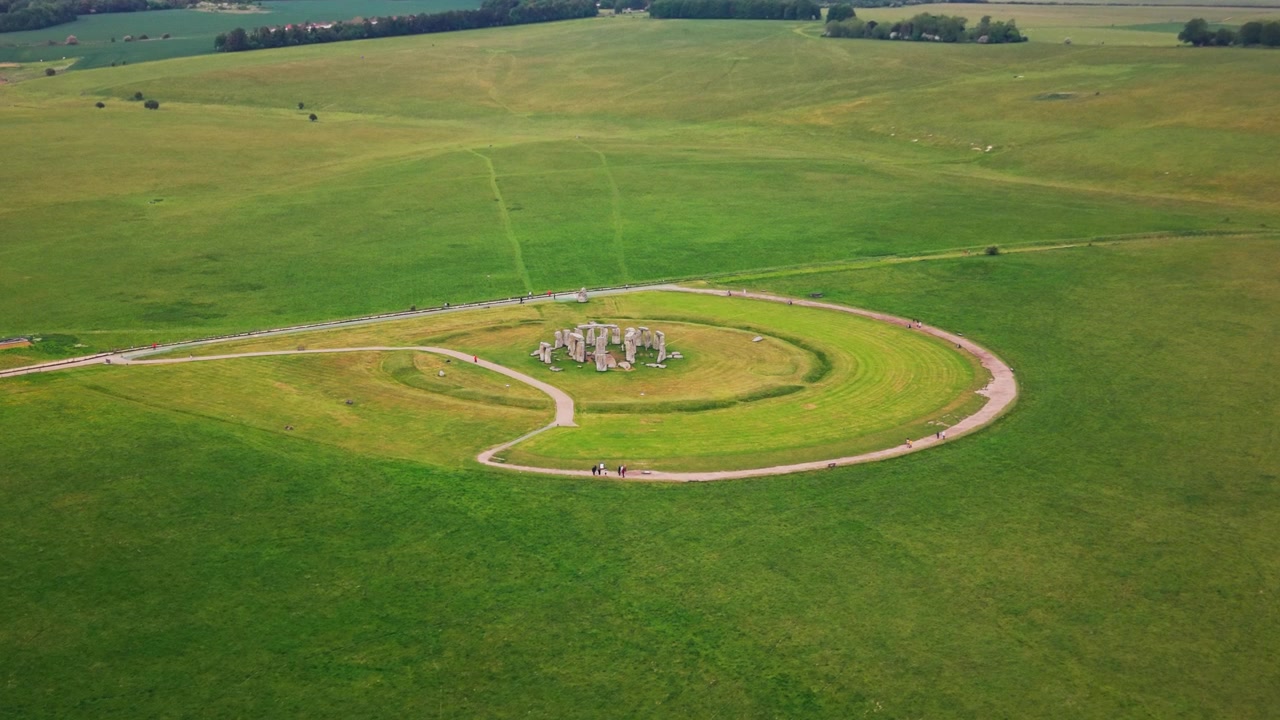 Very wide aerial drone footage of Stonehenge in Wiltshire, England, showing the ancient prehistoric stone circle set within the open green grassland of Salisbury Plain.