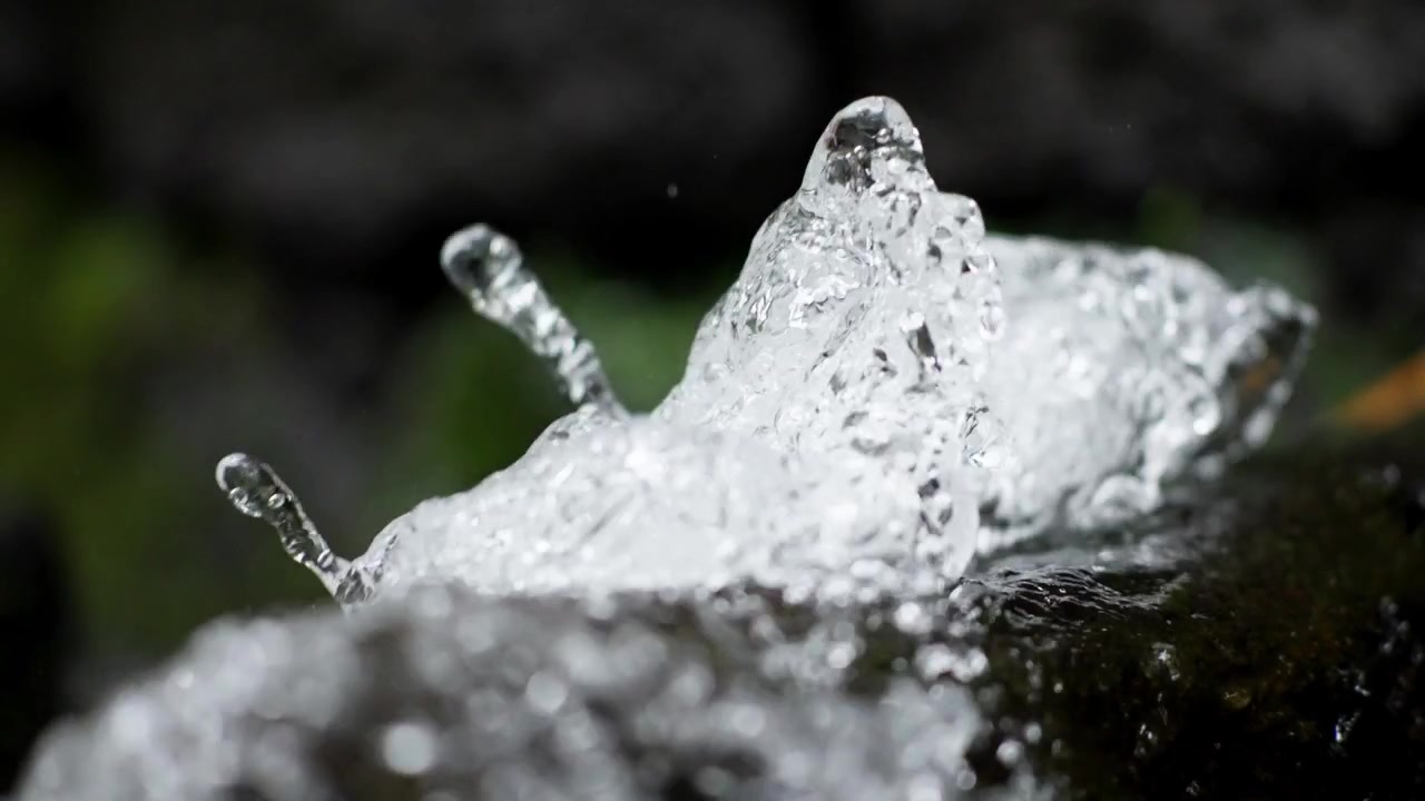 Clear liquid forms dynamic shapes and fast bubbles as it rushes across a wet rock.
