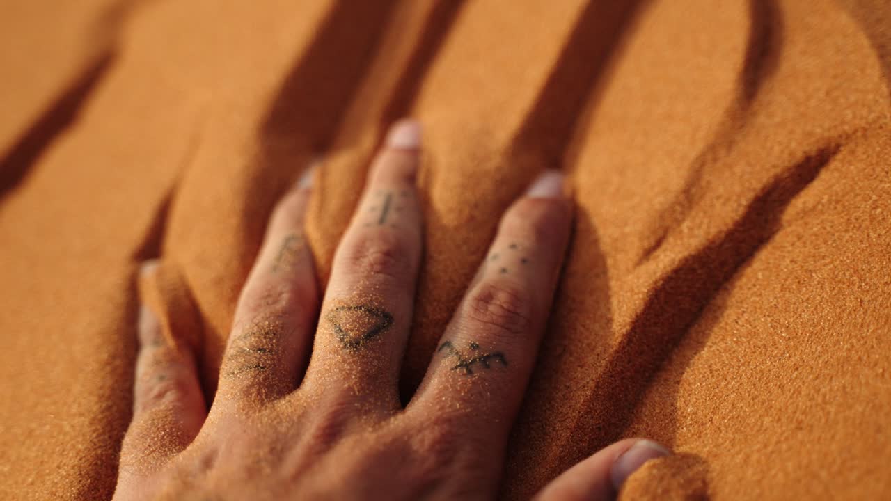 Close-up of a hand gently pressing into fine Sahara desert sand, capturing its golden texture under warm sunlight in Morocco