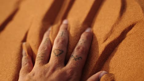 Close-up of a hand gently pressing into fine Sahara desert sand, capturing its golden texture under warm sunlight in Morocco