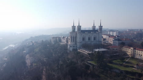 Basilica-of-Notre-Dame-De-Fourvière-aerial-view-overlooking-hazy-Lyon,-French-cityscape-skyline-at-sunrise