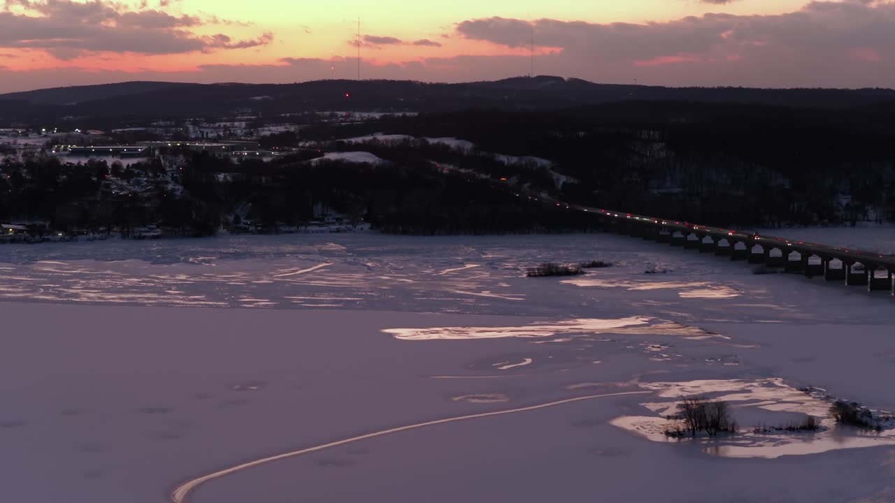 Ilmakuva auringonlaskusta jäätyneestä Susquehanna-joesta Columbian ja Wrightsvillen välillä Pennsylvaniassa, sillan liikenteen, jäisen veden ja kumpuilevien kukkuloiden kera värikkään talvitaivaan alla. Joulunaika. Panoraama.