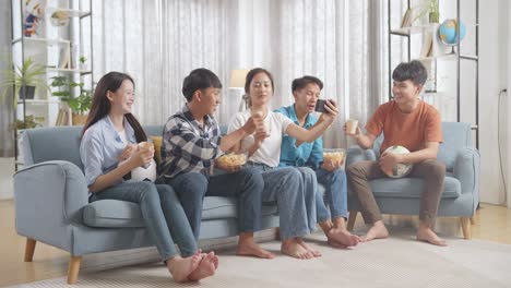 asian teenagers cheering, eating and drink while watching football game on smart phone at home