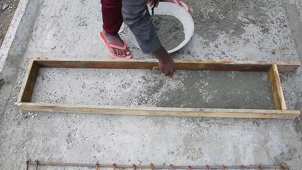 Indian mason worker pouring cement powder into a wooden slab to form a solid foundation for construction