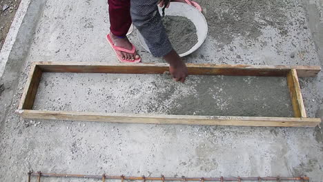 indian mason worker pouring cement powder into a wooden slab to form a solid foundation for construction