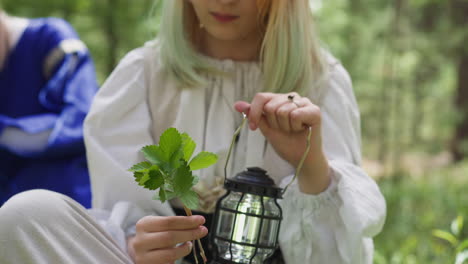 teenage girl in vintage dress looks at leaves holding lamp