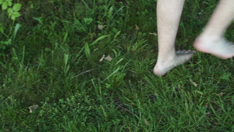 high angle closeup of naked male feet legs walking on lush green grass, pan, day