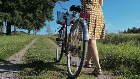 woman in vintage dress walking with bike country road in countryside, crane shot