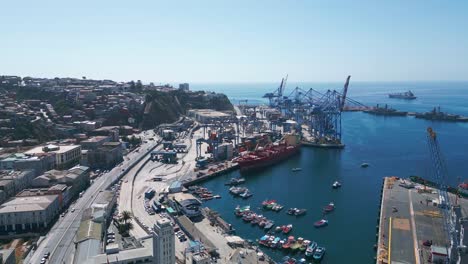 drone flying towars to commercial port with cranes, containers and cargo ships on a sunny day in valparaiso, chile