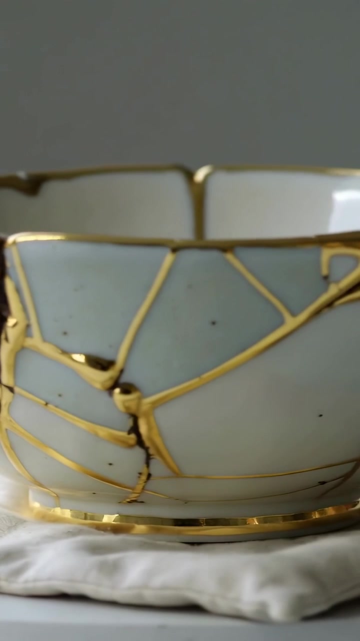 Vídeo vertical: Câmera panorâmica sobre tigela de porcelana em tecido revelando kintsugi dourado e manchas escuras.
