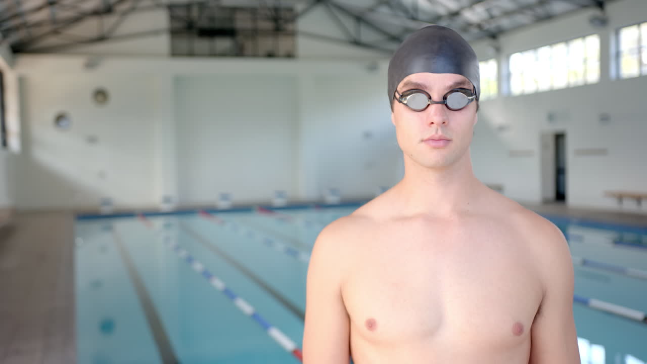 male swimmer wearing swim cap and goggles standing by indoor swimming pool, copy space