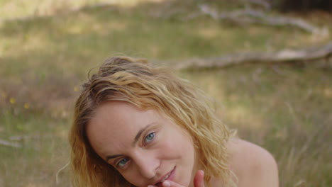 portrait of a pretty woman with blond curly hair being one with nature in a beautiful green forest. the girl enticingly looks at the camera and waves her hair in slow motion