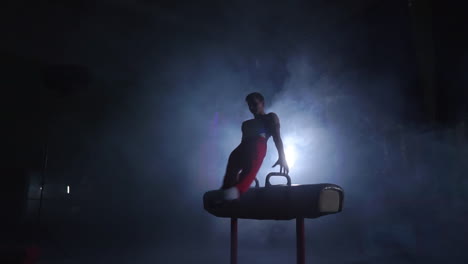 male gymnast performs pommel horse exercise in a dark room in smoke in slow motion. sports for health and achievement