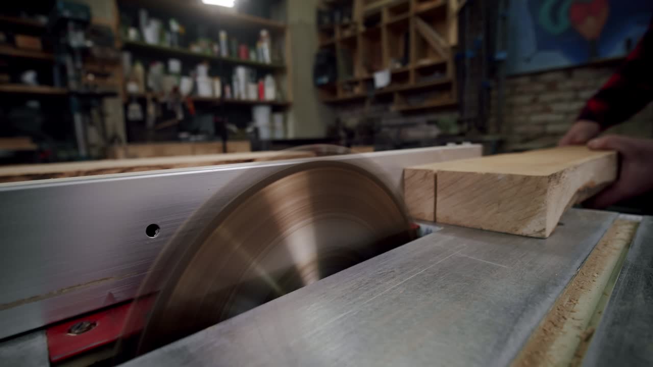 вблизи. мастер разрезает деревянную доску циркулярной пилой в деревообрабатывающей мастерской небольшого производителя мебели. медленное движение. v4
