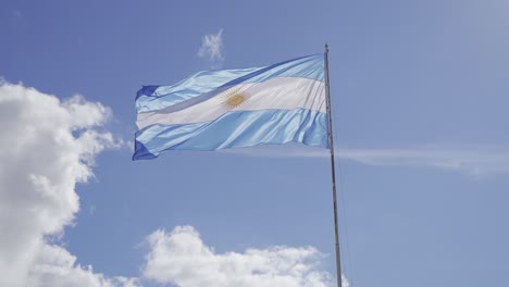 zeitlupenaufnahme der argentinischen flagge, die im sommer gegen blauen himmel und wolken weht - niedriger winkel, 4k