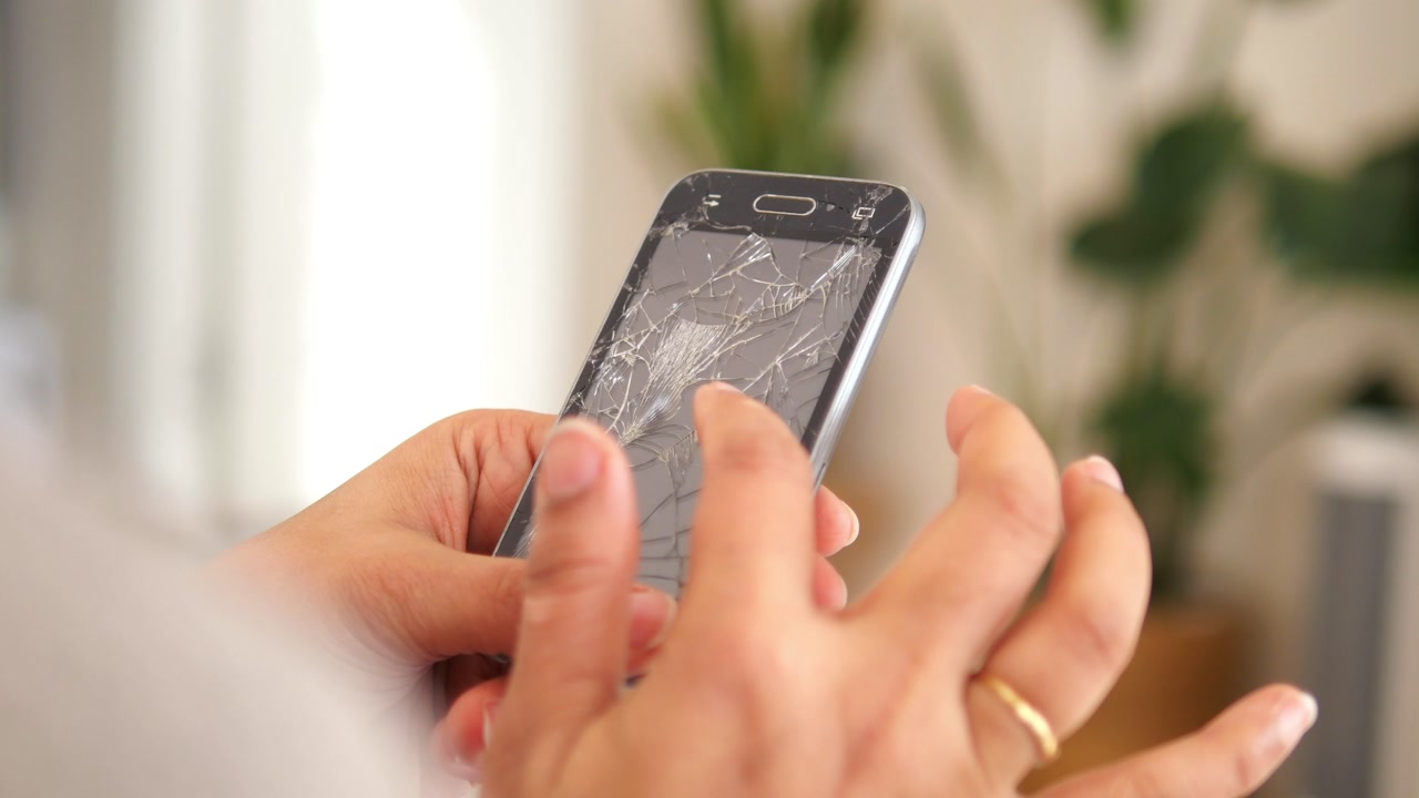 Close-up of Hands Holding a Smartphone with a Cracked Screen