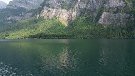 Olas-Tranquilas-Y-Relajantes-Que-Llegan-A-La-Orilla-Del-Lago-Klontalersee-Con-Alpes-Suizos-Rocosos-Que-Abrazan-Las-Costas