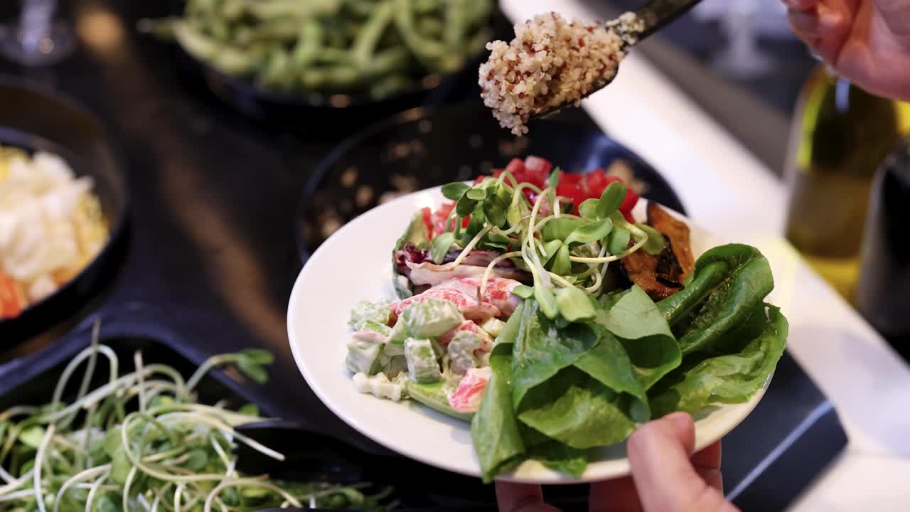 Hand scoops quinoa onto colorful mixed greens salad at a bright, modern salad bar buffet