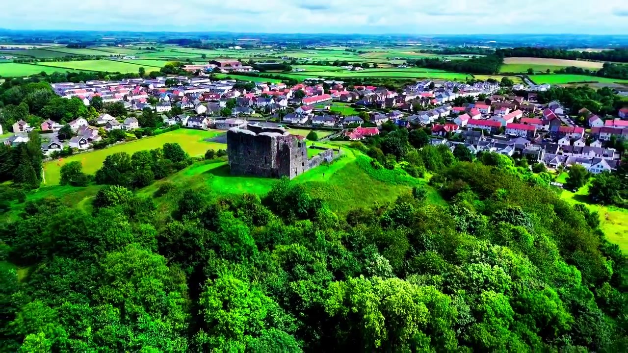Ladera del Castillo de Dundonald rodeada de bosque, edificios de pueblo y campiña ondulada en Ayrshire, Escocia, vista aérea cinematográfica con efecto de revelación