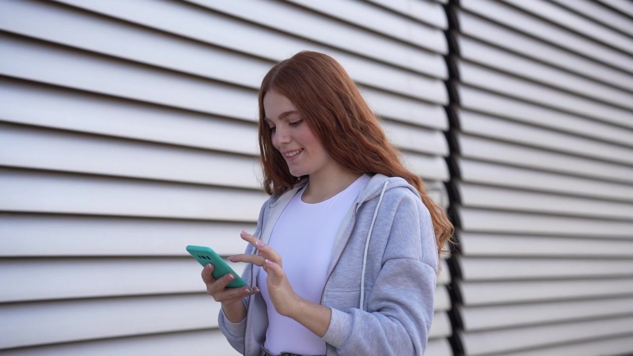 Una giovane donna che si gode felicemente il suo smartphone mentre passeggia tranquillamente all'aperto in città.