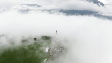 Disparo-De-Drones-Inclinándose-Sobre-La-Iglesia-De-San-Nicolás-En-Medio-De-La-Niebla-En-Renon,-Italia