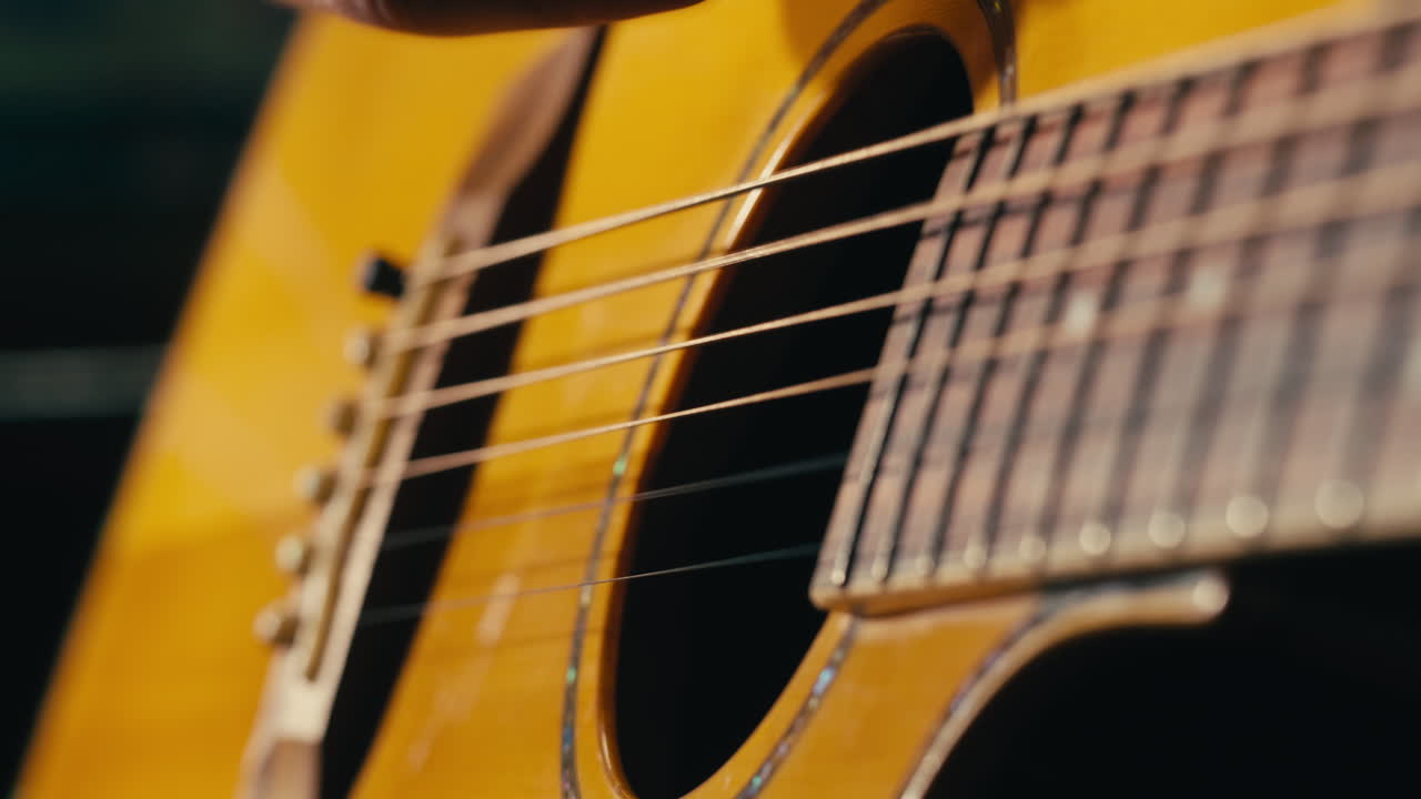 Young musican man checking strings of acoustic guitar close-up. Male guitarist tuning sound of musical instrument.
