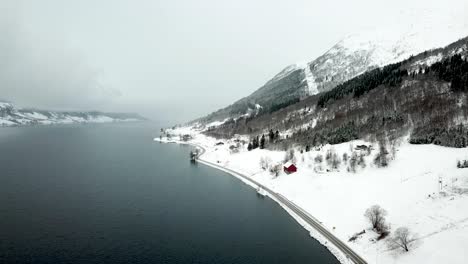 aerial flyover jolstravatnet lake during cold foggy winter day beside overgrown mountains and empty road on shore. skei,norway.