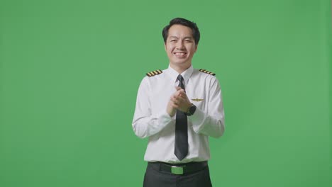 아시아인 조종사가 녹색 스크린 배경 스튜디오에 서서 미소 짓고 손을 치고 있습니다.