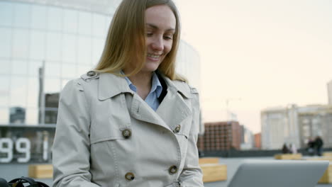 young businesswoman sitting outdoors with laptop on her knees and typing