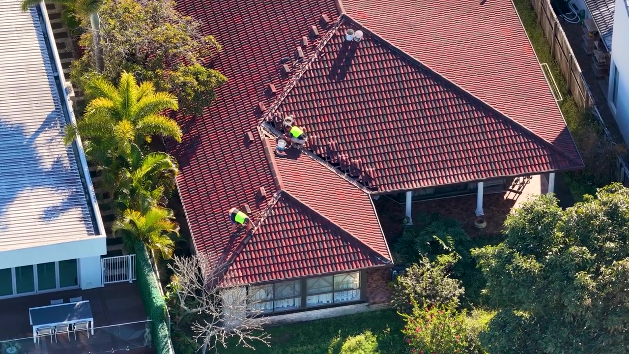 Aerial shot of workers in high-visibility vests performing maintenance on a residential tile roof.