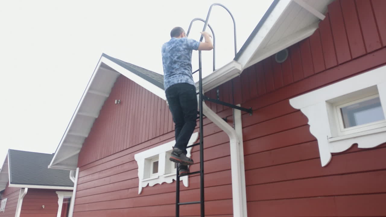 A man climbs a ladder outside a red house in snowy Santa Claus Village, Rovaniemi, Finland