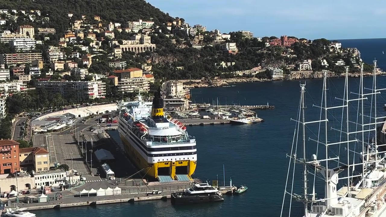 Vista dall'alto di una grande nave da crociera attraccata a Nizza, Francia, circondata da yacht, case sulla collina e il Mar Mediterraneo blu