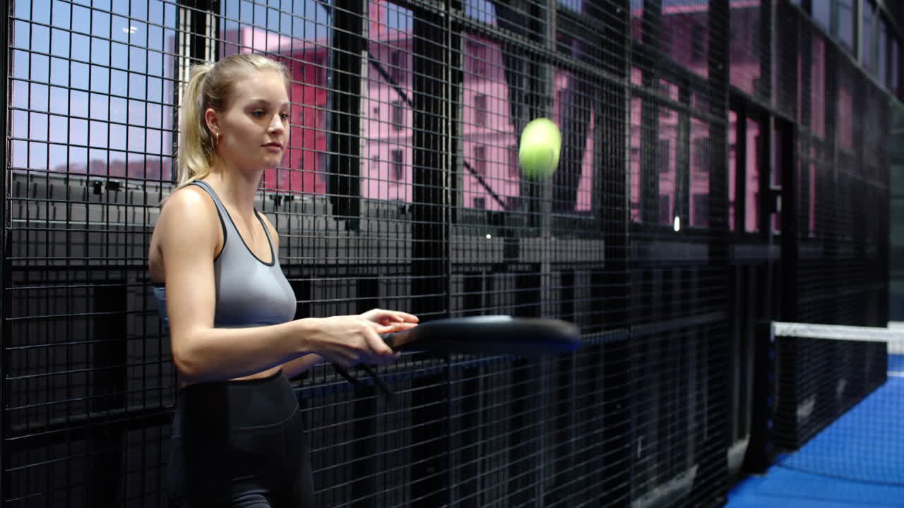 Focused woman holding padel racket and ball, preparing for match in indoor court, copy space