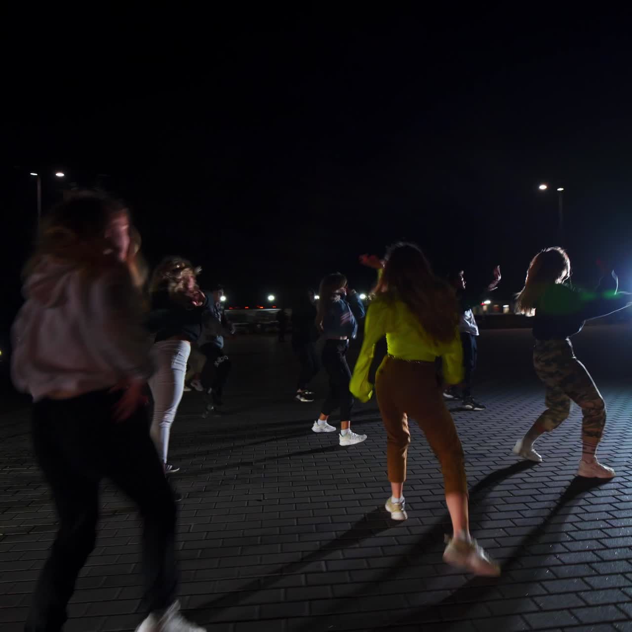 Large group of young people dancing hip hop on the square outdoors at night. Dance group performs in the flashing lights. Cars at backdrop