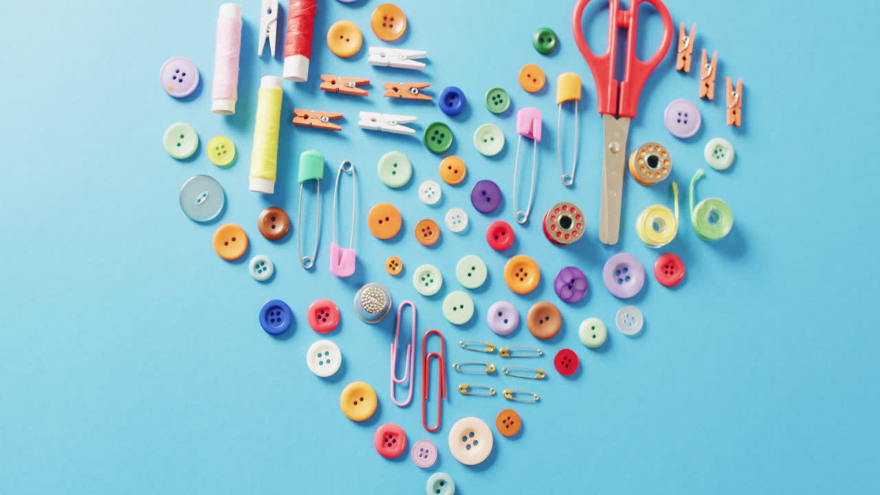 video de tijeras, botones, alfileres, clips, clavijas y bobinas de algodón en forma de corazón sobre fondo azul