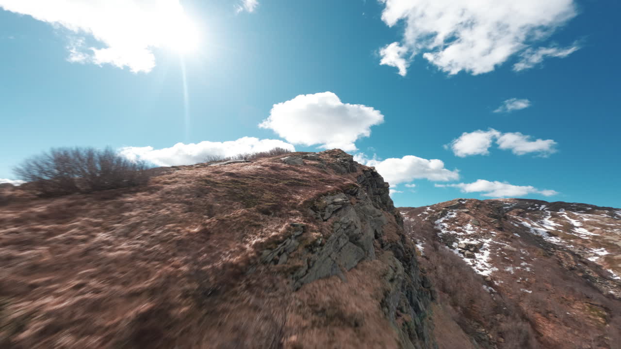 Rugged mountain ridge captured with FPV drone under bright blue sky and clouds