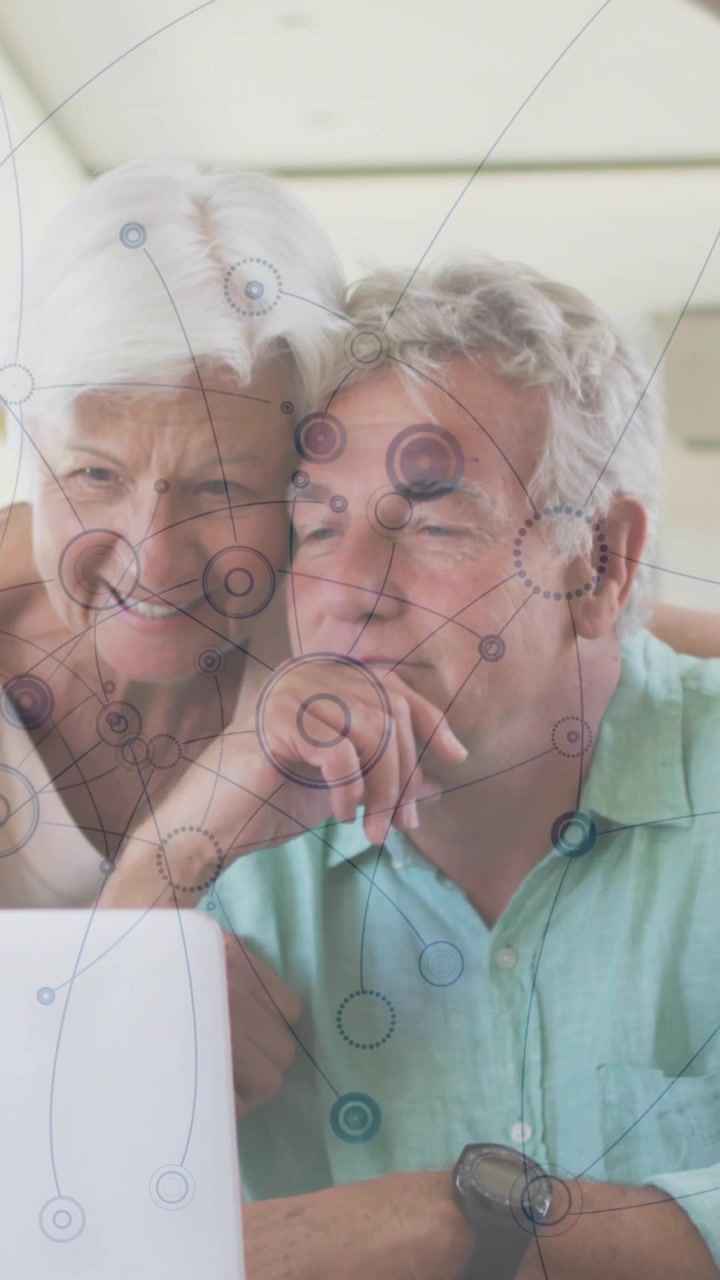 Senior pair sitting, man holding blue disc leaning, pointing at laptop, overlay rising, exploring
