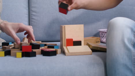 las manos del niño y la mujer jugando con cubos de madera en el sofá en la sala de estar en casa