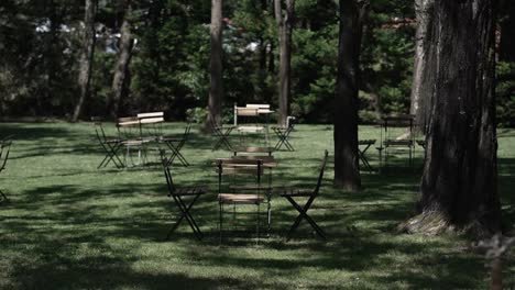 empty outdoor seating area with scattered tables and chairs in a shaded, wooded garden